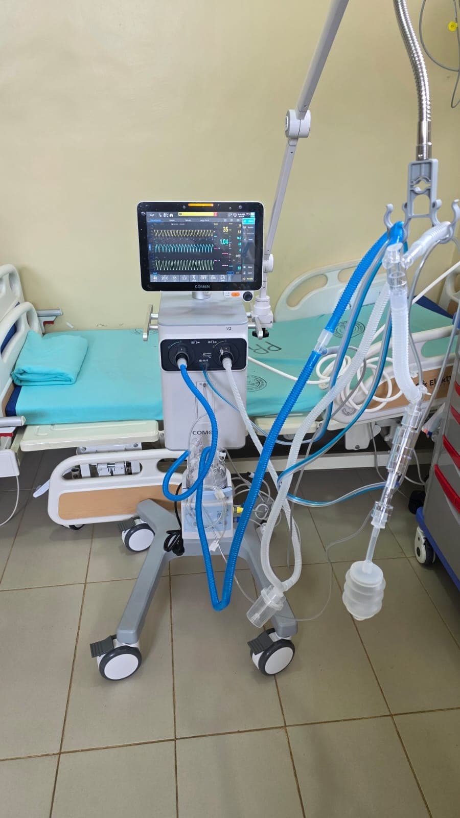Ventilator with patient circuit set up beside a hospital bed on a ward